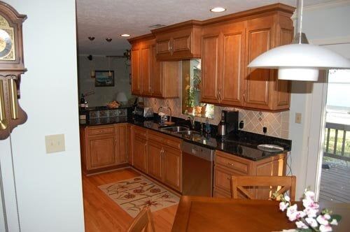 A kitchen with light wood cabinets, dark granite countertops, stainless steel appliances, and wood floors.