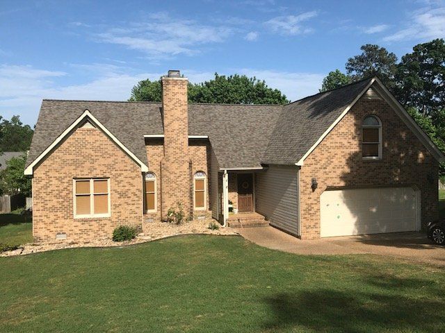 A two-story brick house with a brown shingled roof, a chimney, and a two-car garage on a sunny day.