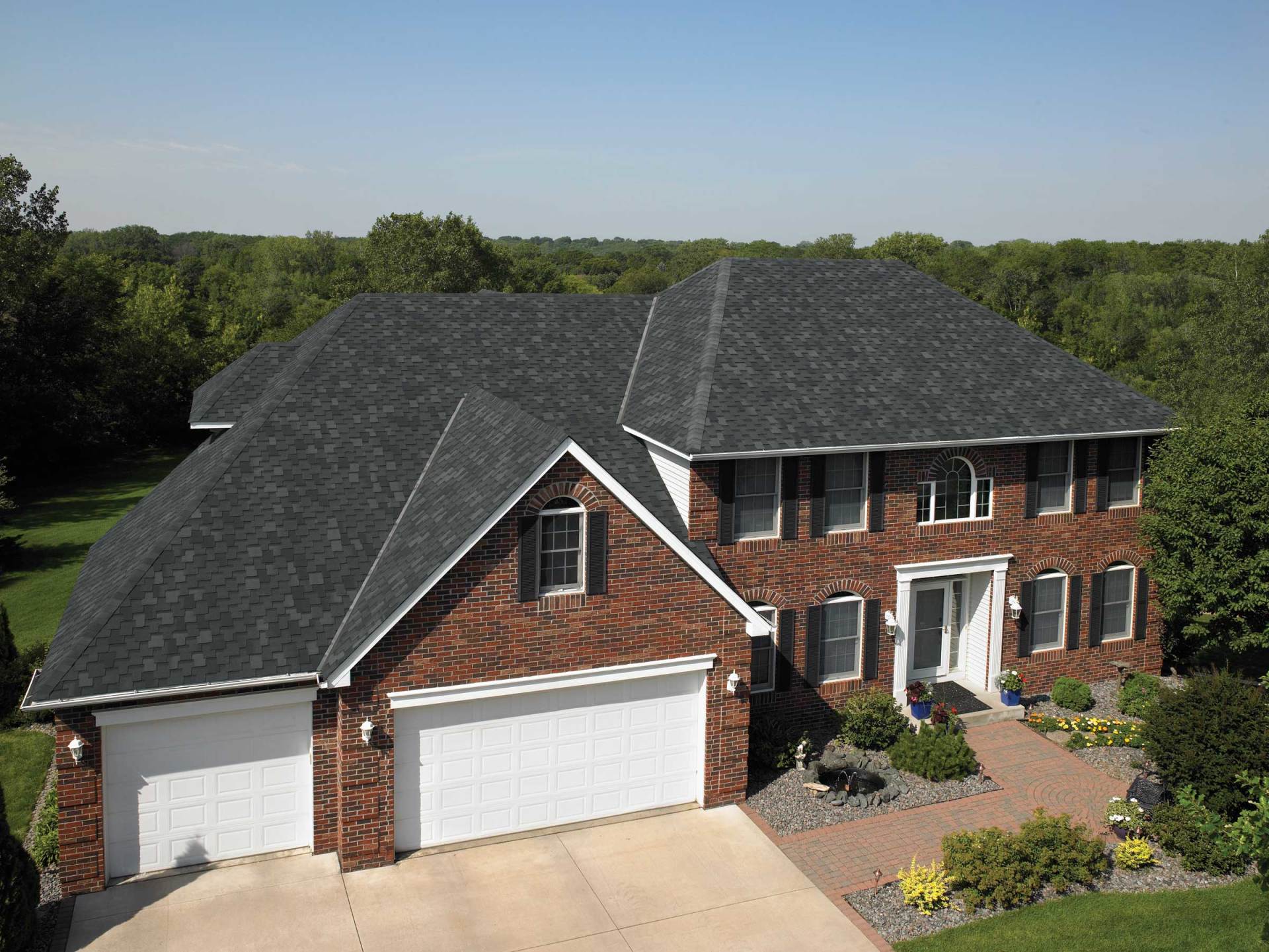 Two-story brick house with a dark shingled roof, a three-car garage, and a landscaped front walkway.
