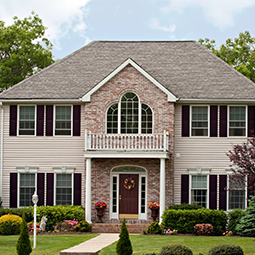 House construction—General Contractor in Newport News, VA A two-story brick and siding house with a central balcony, arched window, and landscaped yard.