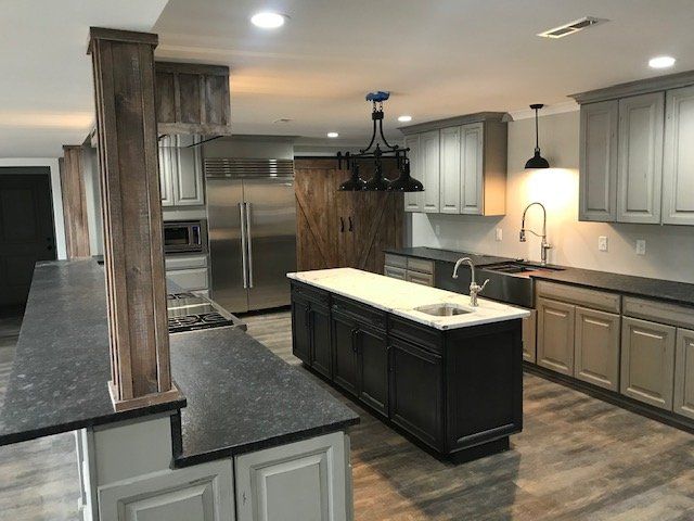 A modern kitchen with grey cabinetry, a black central island, a rustic wooden support column, and stainless appliances.