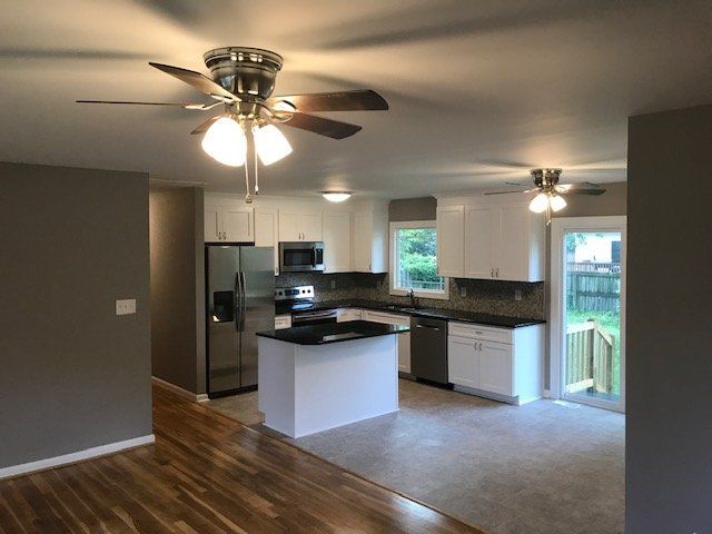 An open-concept kitchen with white cabinets, dark countertops, stainless steel appliances, and a central island.