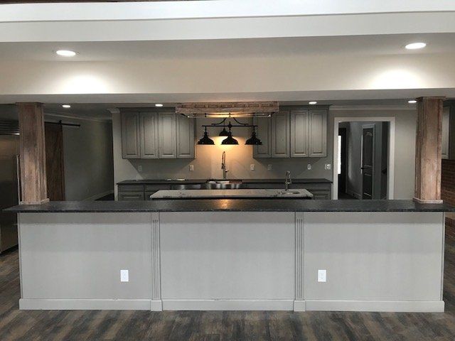 A modern kitchen island with a dark countertop and light grey base sits in front of wood-trimmed columns and cabinetry.