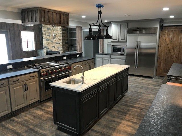 A modern kitchen with a dark central island, gray cabinets, stainless appliances, and a rustic wood-paneled feature wall.