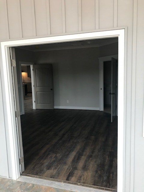 A doorway showing a view into a room with gray walls and dark wood-look flooring, with two open doors leading to other rooms.