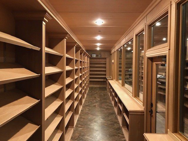 A narrow hallway lined with wooden shelving units, wooden trim, and a dark tiled floor under recessed ceiling lighting.