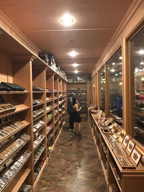 A narrow aisle inside a cigar shop with wooden shelves filled with boxes of cigars lining both sides.