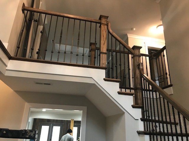An indoor staircase with dark wood handrails and dark metal balusters leading to an upper landing in a modern home.