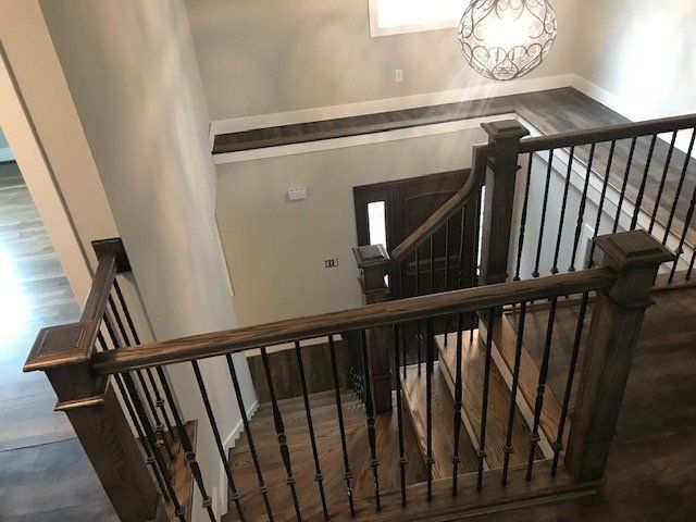 A view from the top of a wooden staircase featuring dark railings with black iron spindles looking down toward an entry.