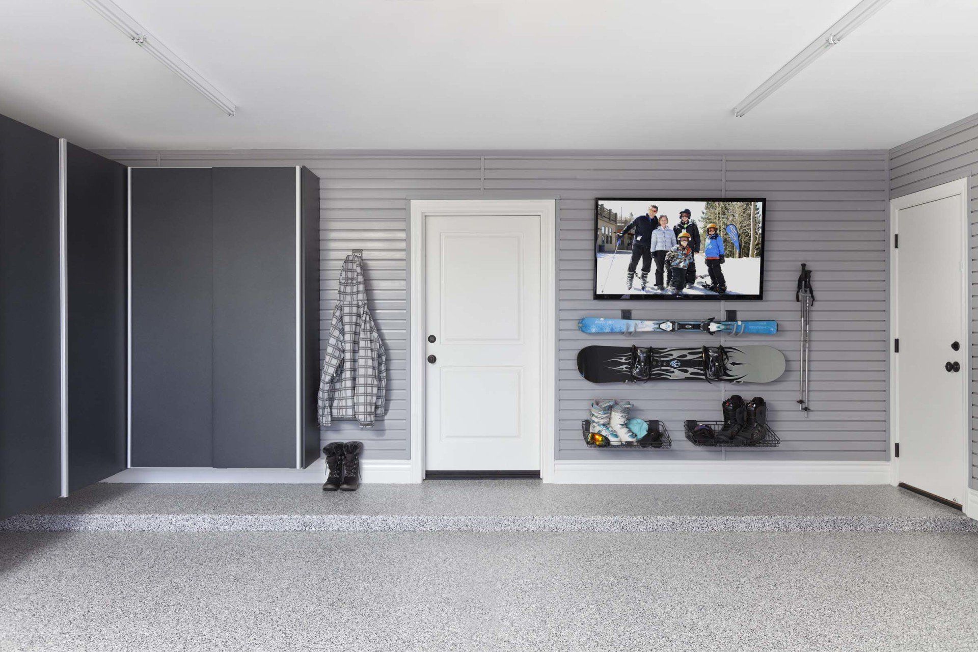 A garage with a tv on the wall and snowboards hanging on the wall.