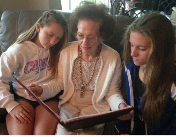 Three people sit on a couch looking at a photo album together.