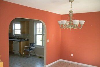 Empty dining room with coral walls, arched doorway, chandelier, and a glimpse of the kitchen beyond