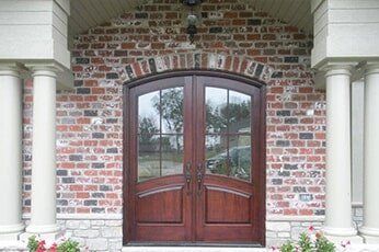 Double wooden front doors in a brick entryway with white columns