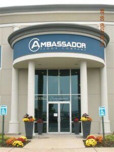 Ambassador building entrance with blue sign, white columns, glass doors, and flower planters