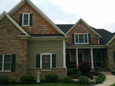 Suburban house exterior with stone and green siding, dormer windows, and a curved front walkway