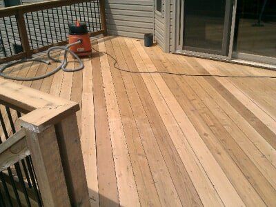 Wooden deck with railing, sliding door, hose, and orange power tool near the house
