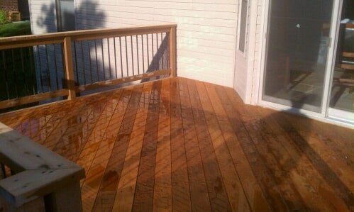 Wooden deck with railing beside a sliding glass door in sunlight