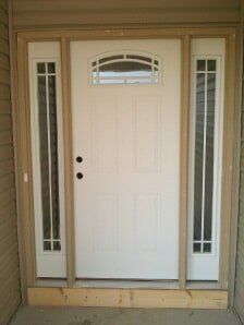 White front door with narrow side windows and an arched window above, framed by tan trim.