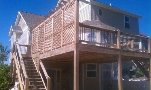Raised house with tan lattice siding, wood deck, and exterior stairs under a clear blue sky