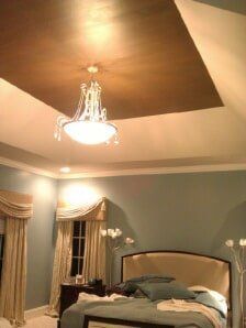 Elegant bedroom with blue walls, chandelier, draped windows, and a large bed under a vaulted ceiling