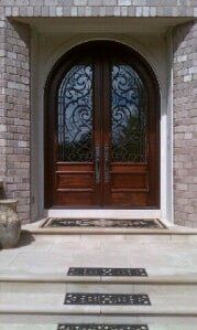 Wooden double front door with ornate glass panels, framed by stone steps and a white entryway.