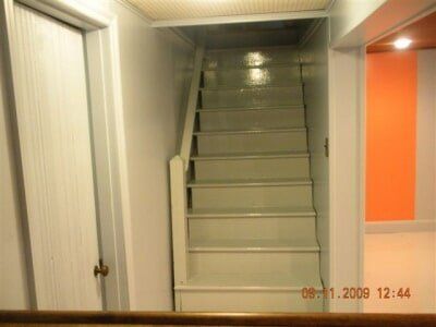 Staircase in a narrow hallway with white walls and an orange door panel on the right.