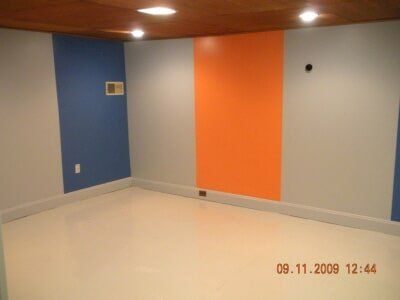Empty room with blue, orange, and gray walls, white floor, and wood-paneled ceiling.