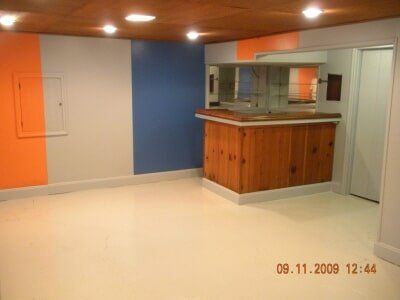 Empty room with orange and blue walls, a wood counter, and a pass-through window around a kitchenette.