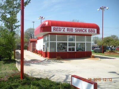 Red and white Red’z Rib Shack BBQ restaurant with awning, windows, and parking lot outside