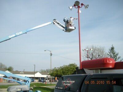 Utility worker in a blue lift fixing a red streetlight pole on a clear day