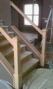 Wooden staircase under construction with unfinished railings in a room with a window and ladder.