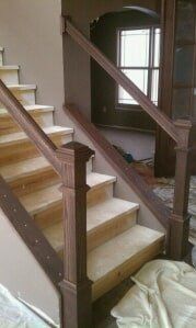 Partially finished staircase with wooden railings and beige steps beside a window