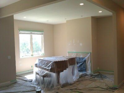 Unfinished room with plastic-covered furniture, exposed wires, and a window letting in daylight
