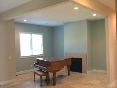 Empty living room with a grand piano, beige walls, fireplace, and recessed ceiling lights