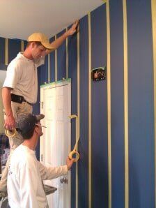 Two people taping blue-and-yellow stripes on a wall during painting or decorating work