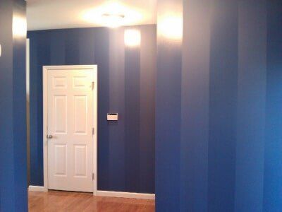 Blue hallway with white door, wall sconce lights, and striped blue painted walls