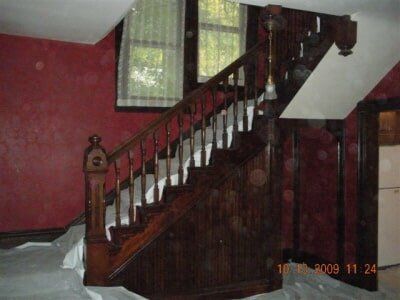 Wooden staircase with dark banister in a red-walled room by a window