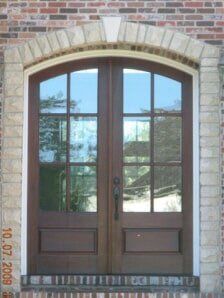 Brown double front door with arched brick surround and glass panes