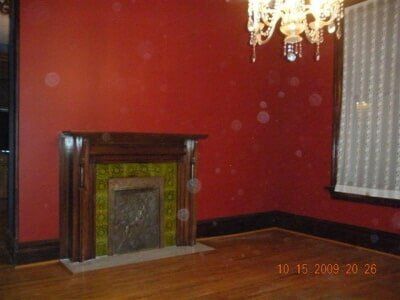 Red-walled room with a fireplace and chandelier, wooden floor, and window blinds.