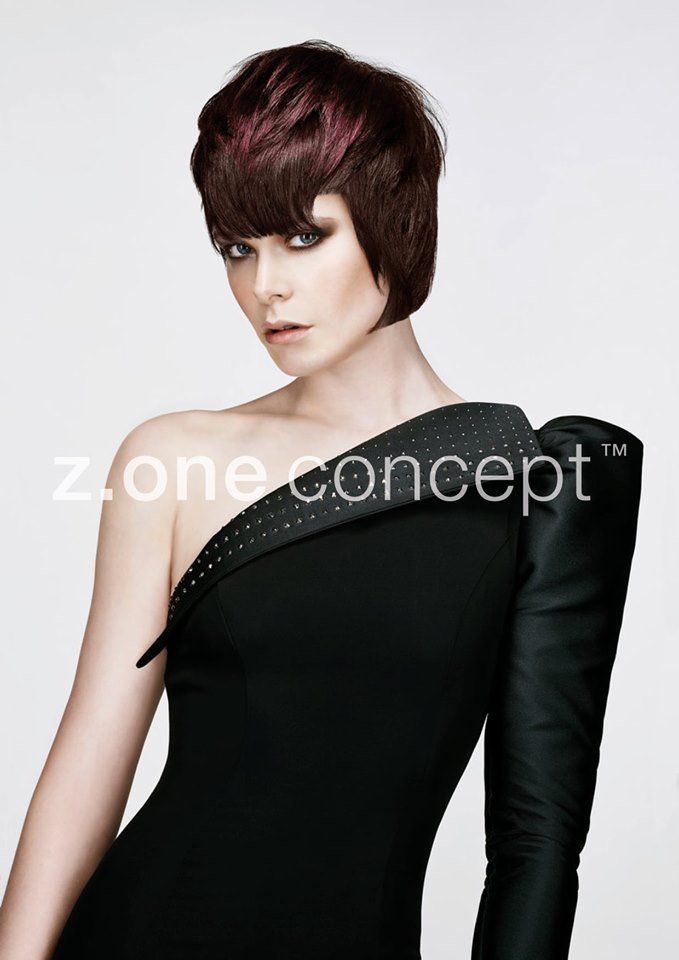 Mujer con cabello corto, color burdeos y castaño, con un vestido negro de un solo hombro; fondo blanco.