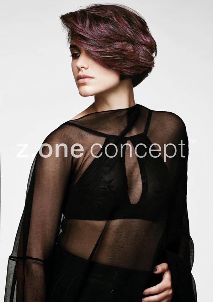 Mujer con cabello corto, en capas y morado. Lleva un top negro transparente. Fondo blanco.