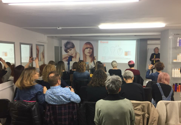 Un grupo de personas asisten a una presentación en un salón, con un orador en el escenario y una imagen proyectada.