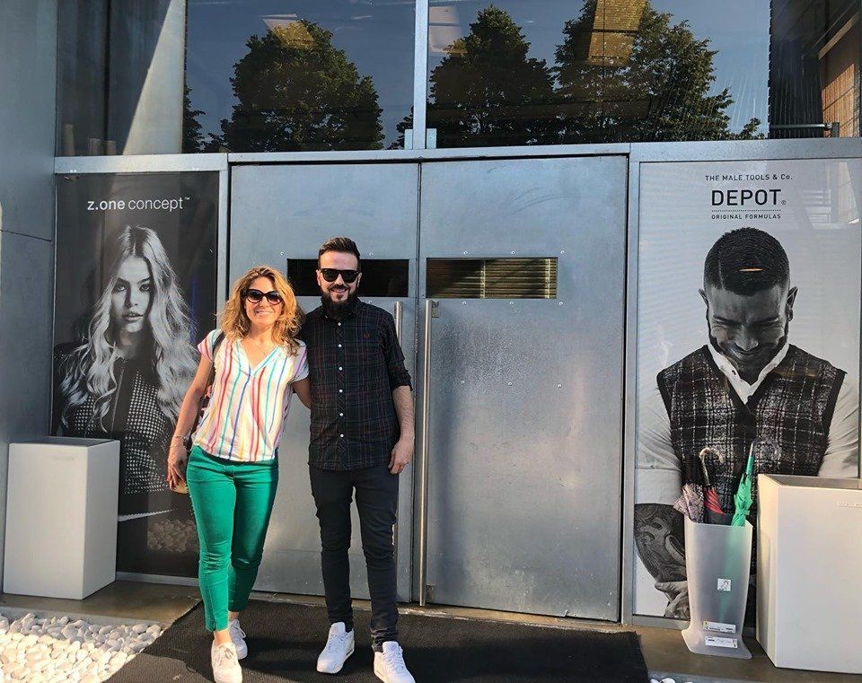 Un hombre y una mujer posan afuera de un salón con carteles publicitarios.