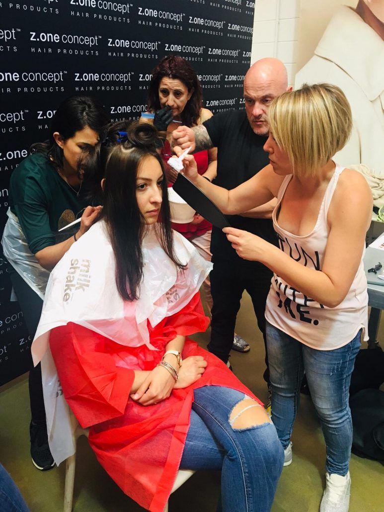 Peluqueros cortando el pelo a una mujer en un salón. Varias personas trabajan en el cabello de la mujer.