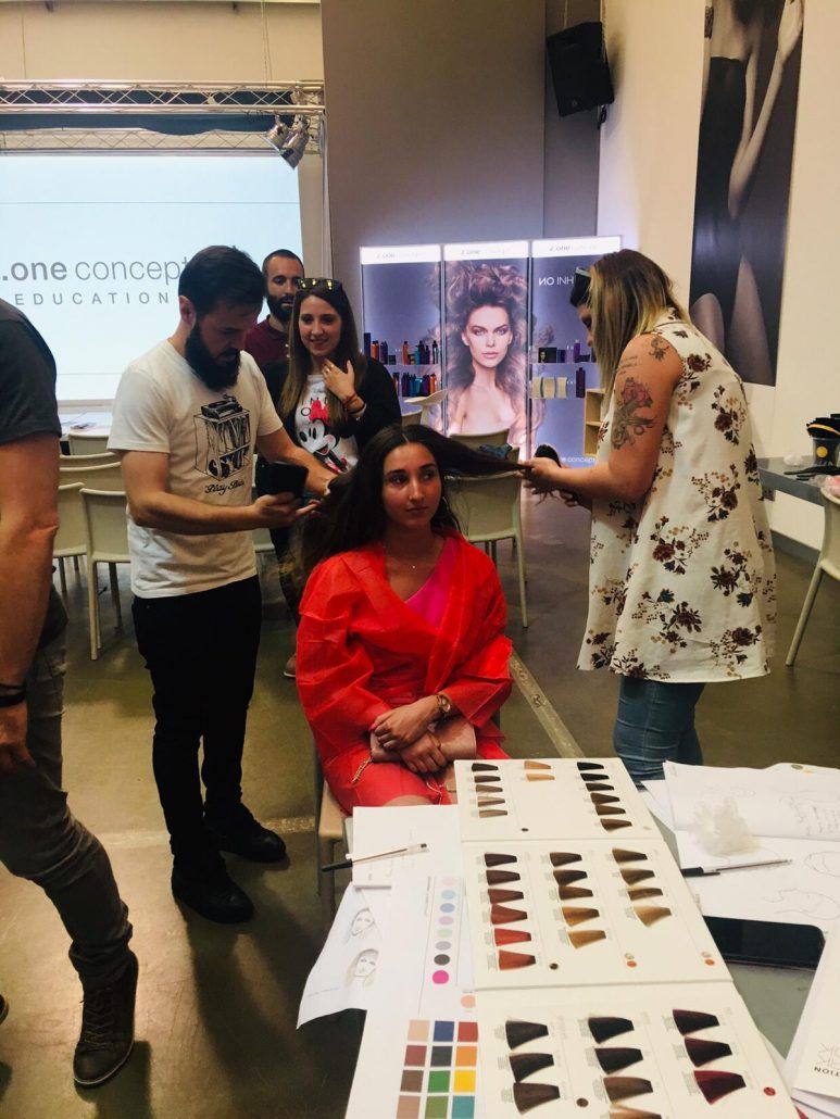 Capacitación en color de cabello: estilistas examinando muestras de cabello cerca de un cliente sentado.