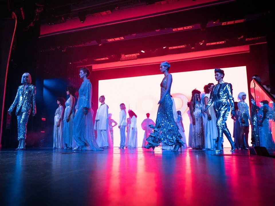 Modelos con vestidos futuristas plateados y vaporosos en el escenario, iluminación roja y azul.