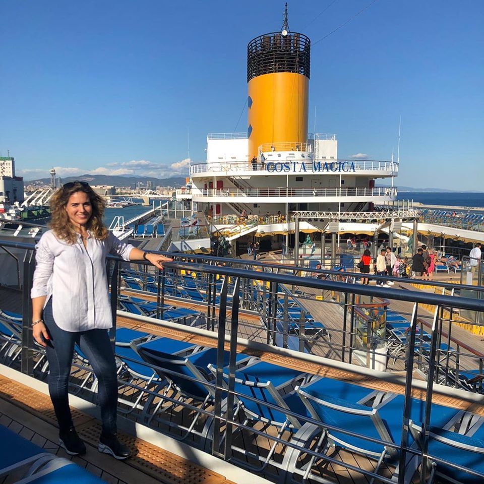 Mujer en la cubierta de un crucero, cielo azul. Chimenea amarilla al fondo, vistas al océano.