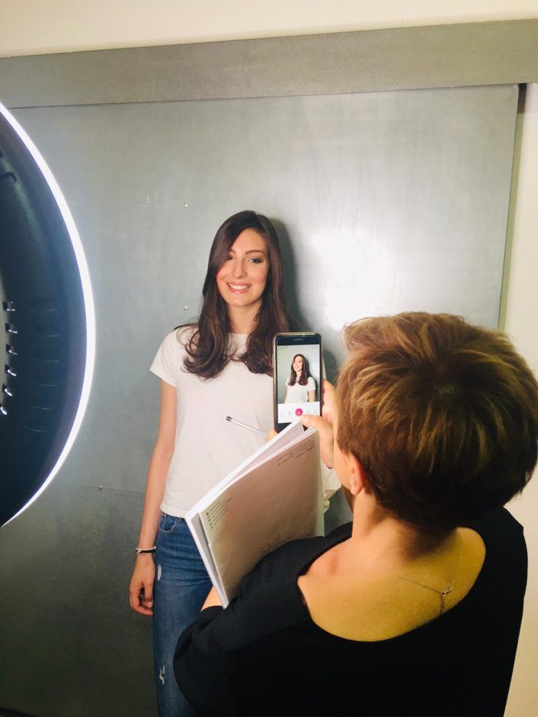 Una mujer posa para una foto con un smartphone y un aro de luz a un lado. Otra mujer le toma una foto.