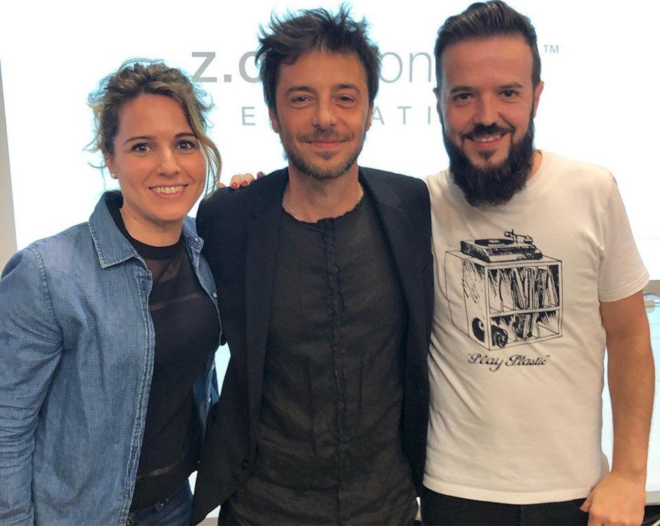 Tres personas sonriendo, posando juntas en un interior. Una mujer con chaqueta