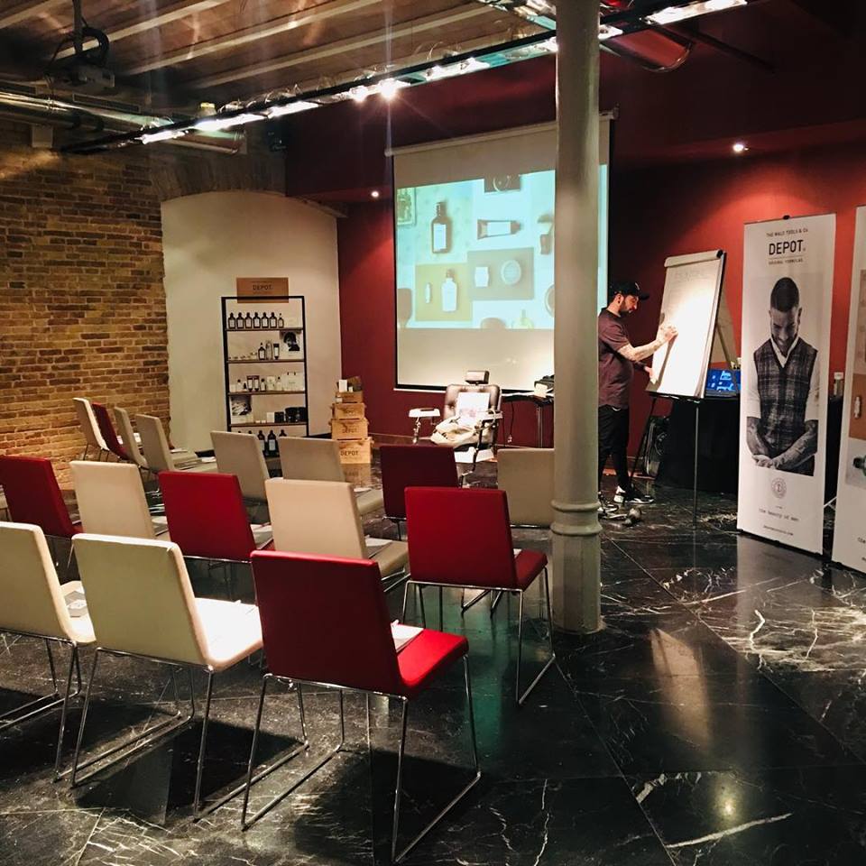 Una presentación en una sala con sillas rojas y blancas. Un hombre escribe en una pizarra.